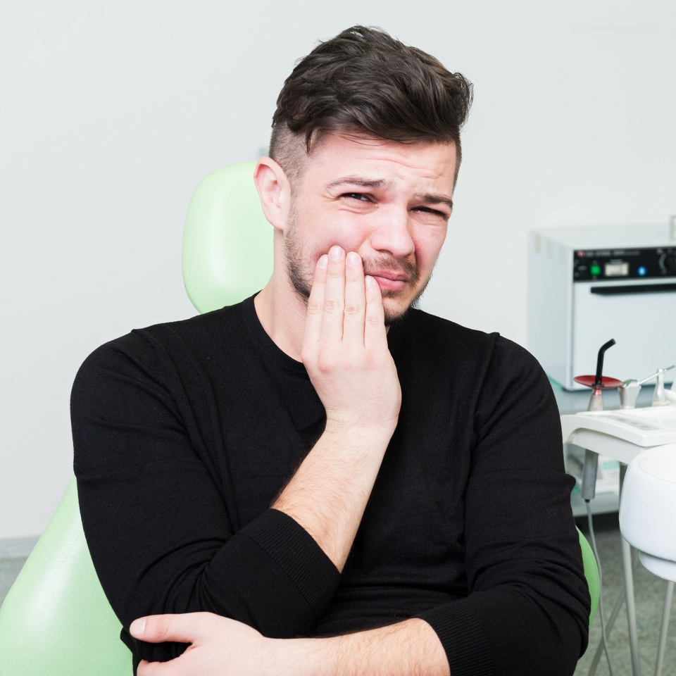 Young man suffering of toothache and pressing his cheek because of pain
