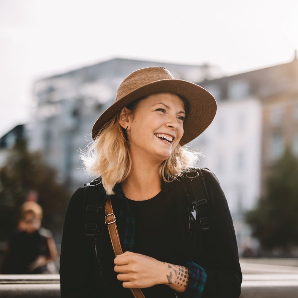 Smiling young woman on a holiday. Tourist woman with a bag wearing a hat on a vacation.