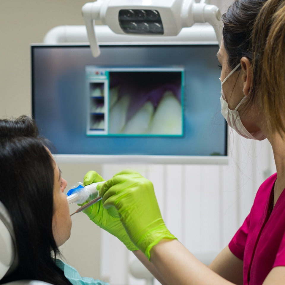 Dentist at work examining woman's teeth in dental clinic with remote camera. Picture of teeth is on the screen. Patient is watching her teeth image. New dental technologies.
