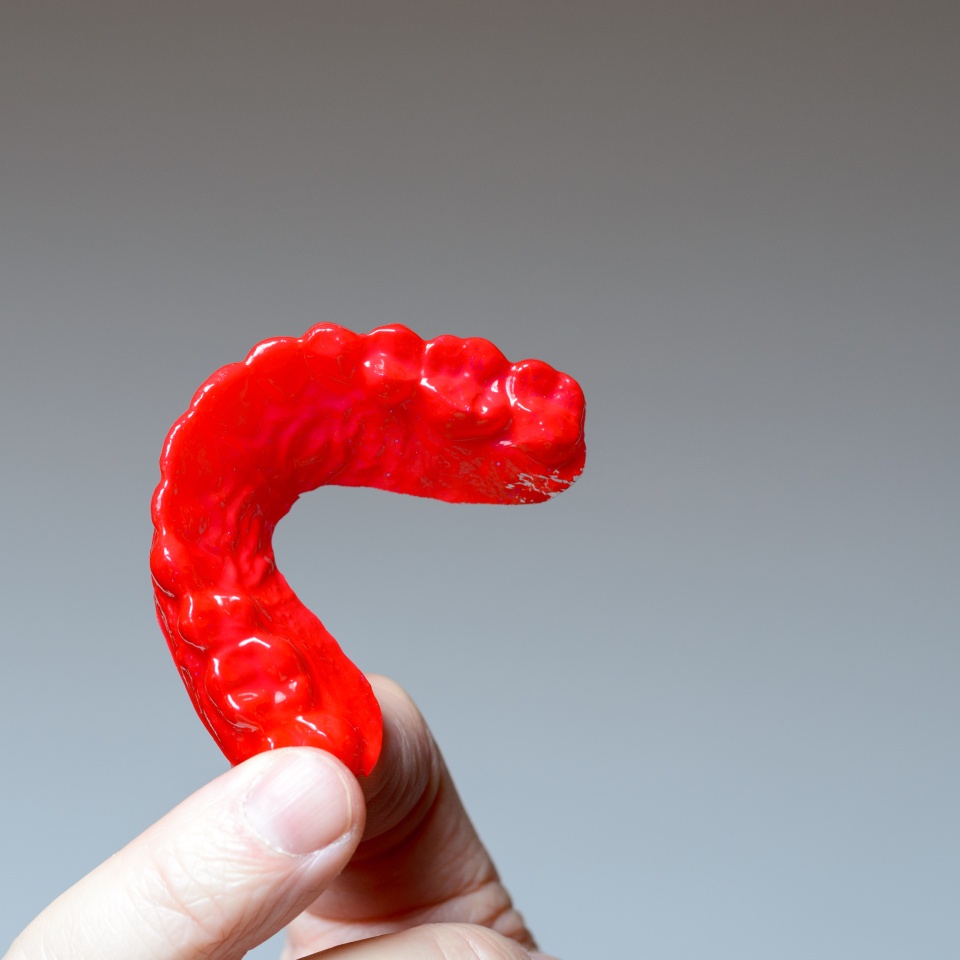 Finger holding a red bite plate to protect his teeth at night from grinding caused by bruxism