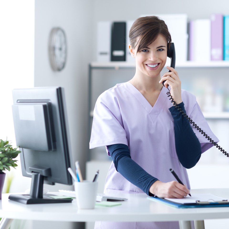 Young practitioner doctor working at the clinic reception desk she is answering phone calls and scheduling appointments