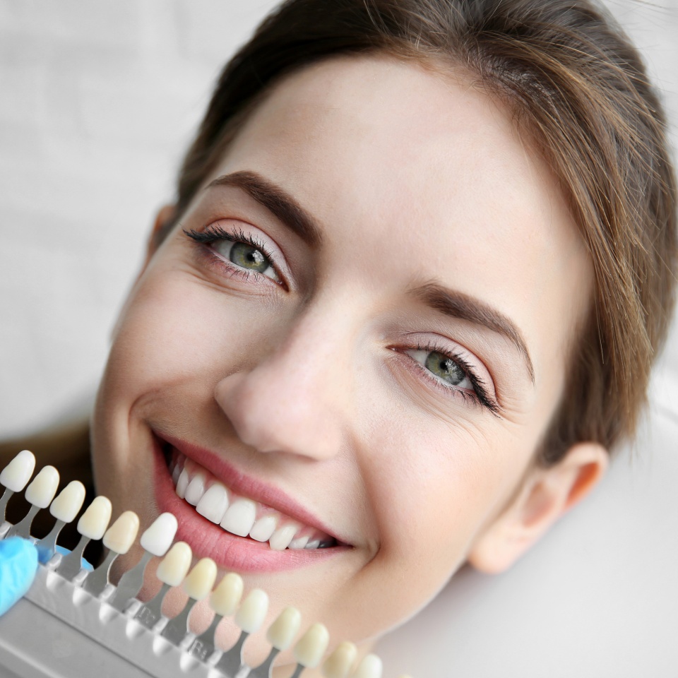 Young woman choosing color of teeth at dentist