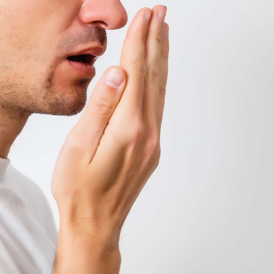 Bad breath. Halitosis concept. Young man checking his breath with his hand.