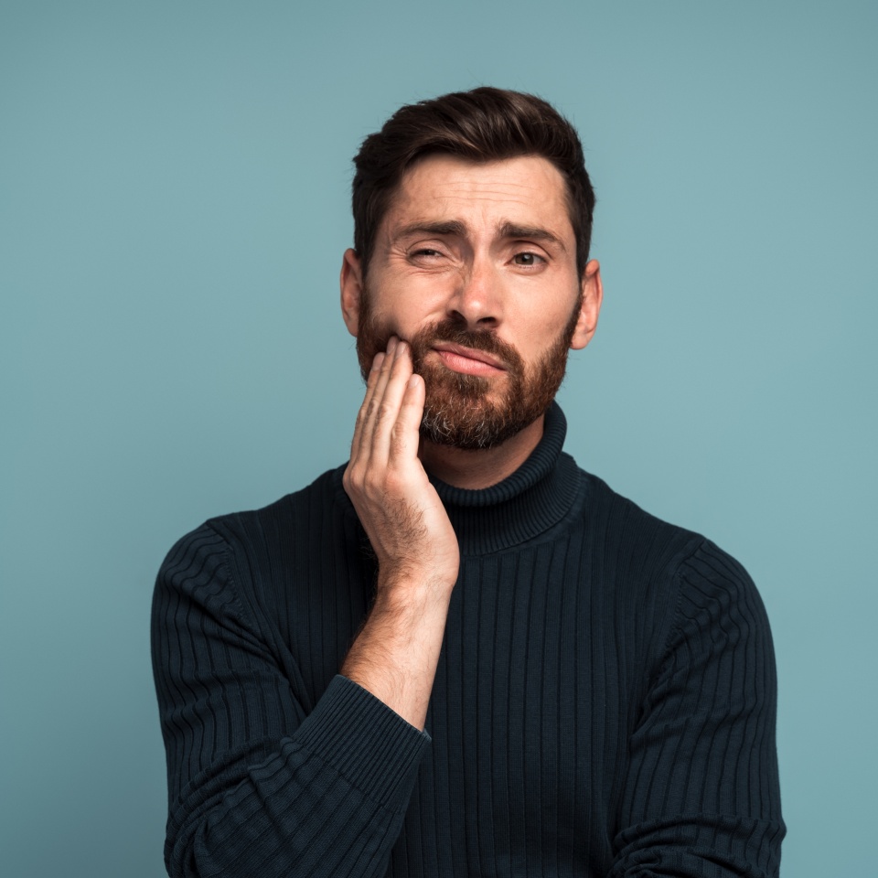 Dental problems. Portrait of unhealthy man pressing sore cheek, suffering acute toothache, periodontal disease, cavities or jaw pain. Indoor studio shot isolated on blue background