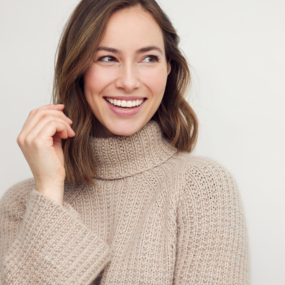 Portrait of young happy beautiful woman smiling and standing isolated on white background in a warm sweater. Young female girl with a perfect smile looking right.