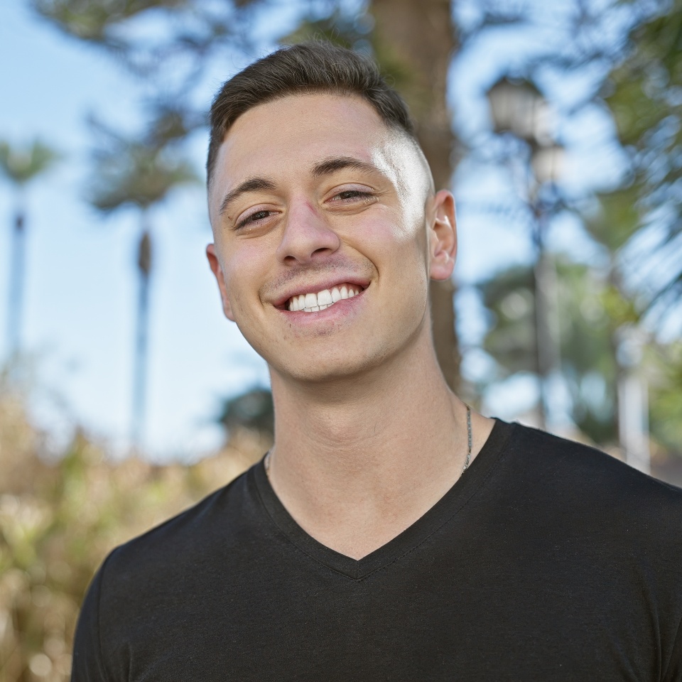 Handsome hispanic man smiling outdoors in a city park with greenery.