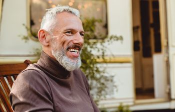 Cropped side view portrait of a good-looking smiling aged man having a break on deck chair near the van. Solo traveler adventurer explorer on a trip by trailer motor home