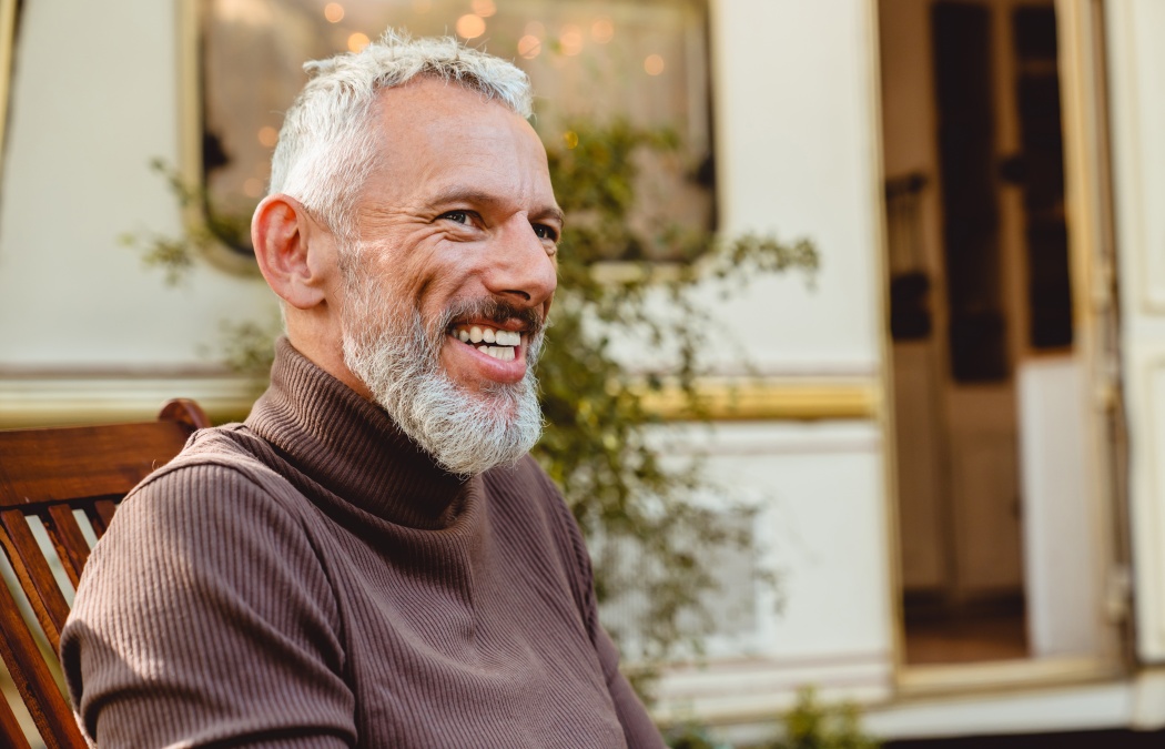 Cropped side view portrait of a good-looking smiling aged man having a break on deck chair near the van. Solo traveler adventurer explorer on a trip by trailer motor home
