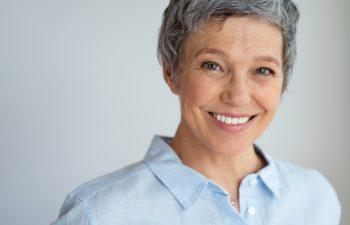 Portrait of happy senior woman isolated against gray background with copy space. Closeup face of confident business woman smiling. Successful businesswoman with a friendly smile looking at camera.